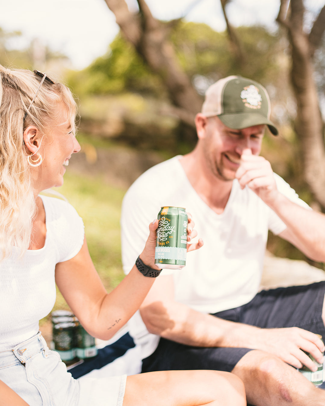 Two people sitting outdoors, one holding a sunday road can