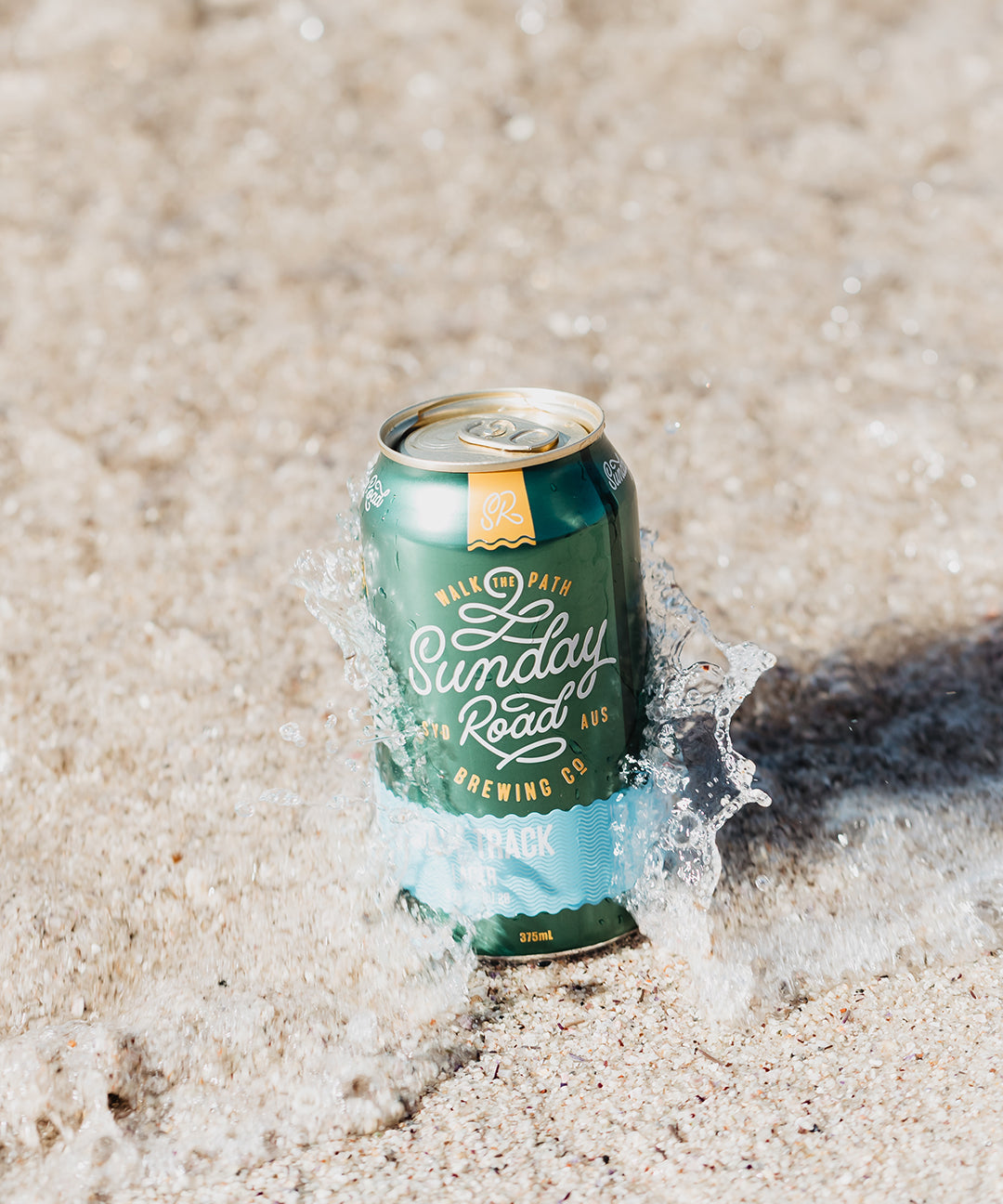 Can of Sunday Road Brewing Coast Track Lager beer on sand with water splash in Cronulla