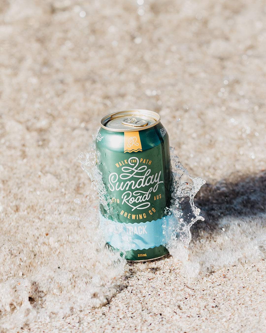 Can of Sunday Road Brewing Coast Track Lager beer on sand with water splash in Cronulla
