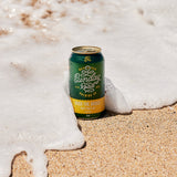 Can of Sunday Road Brewing beer on sand with ocean foam at wanda beach over the bridge hazy pale ale