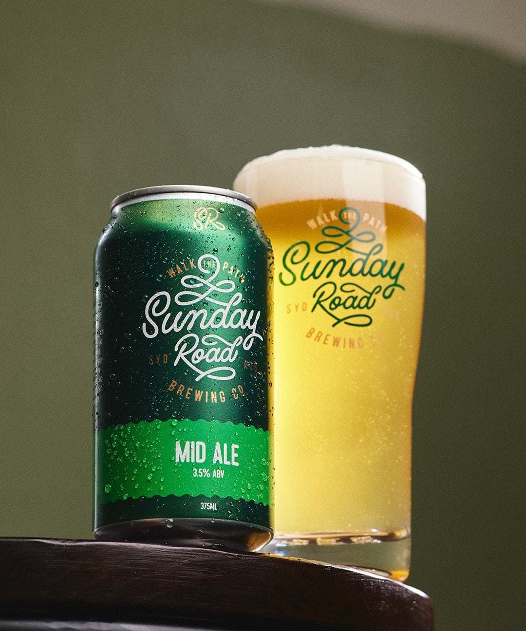 Green can and glass of Sunday Road Mid Ale on a wooden surface with a green background in kirrawee taproom
