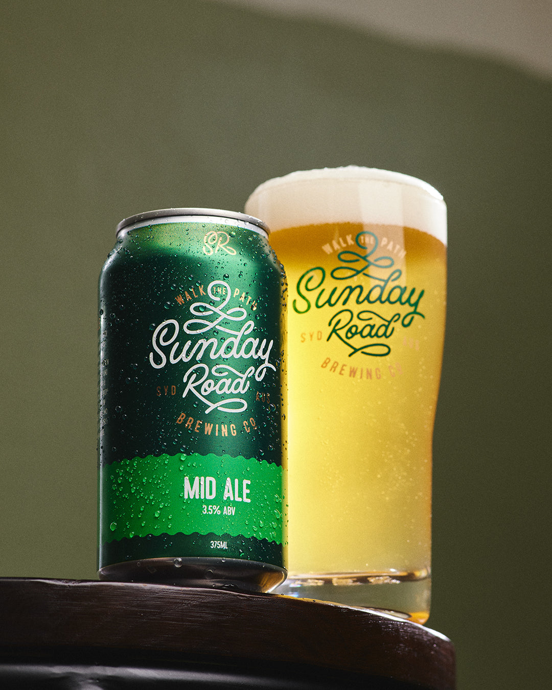Green can and glass of Sunday Road Mid Ale on a wooden surface with a green background in kirrawee taproom