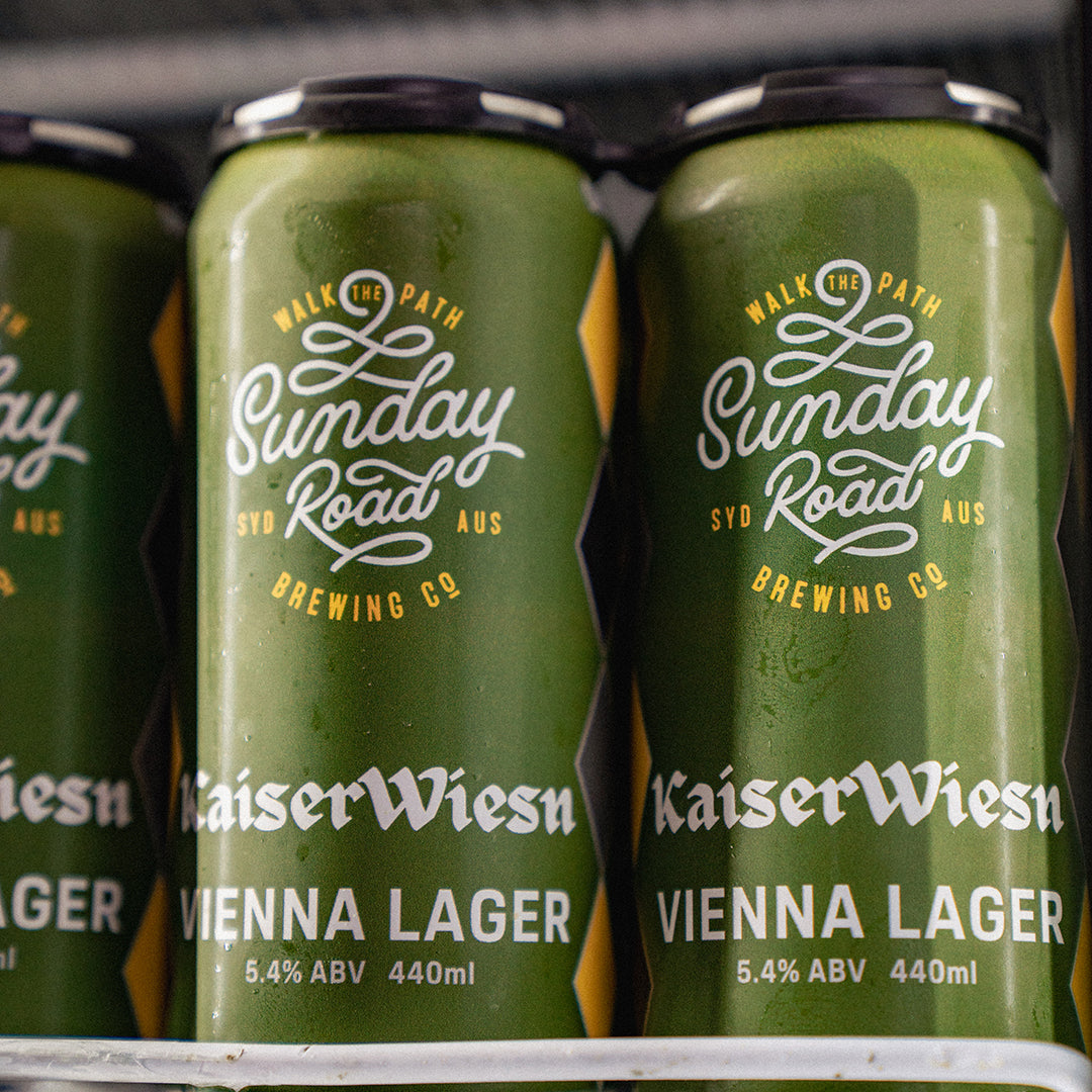 Three green cans of Sunday Road Kaiser Wiesn Vienna Lager in the fridge